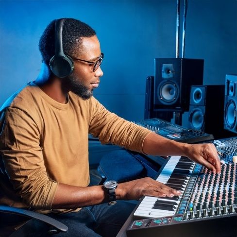 Musikproducent med hörlurar arbetar vid mixerbord och keyboard